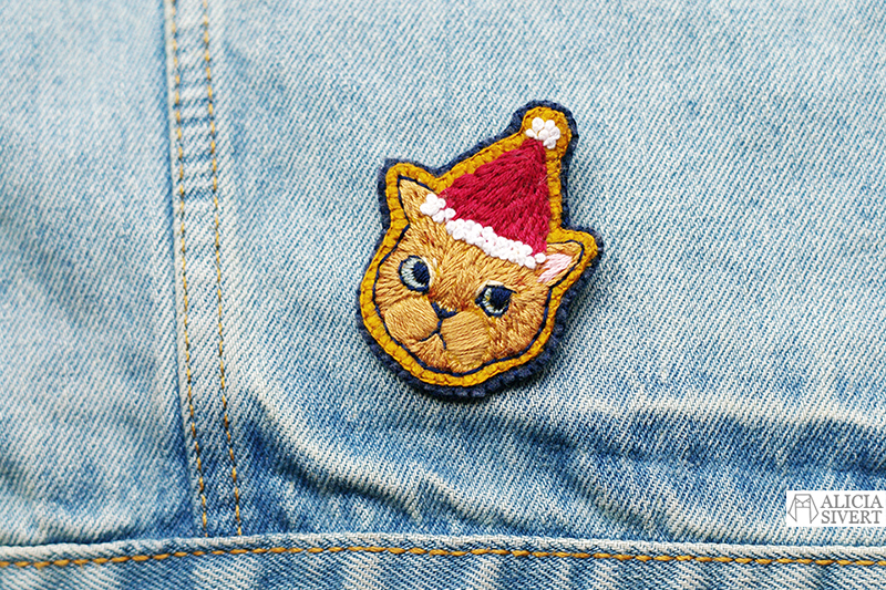 Lussekatt, broderad brosch av katt i tomteluva, av Alicia Sivertsson. / Embroidered Christmas cat brooch by Alicia Sivertsson. aliciasivert alicia sivert sivertsson broderi broderier embroidery hand needlework fritt skapa skapande kreativitet konst textil textilkonst schattérsöm broderad brosch embroidered brooch christmas cat julkatt jul katt tomteluva lussekatt